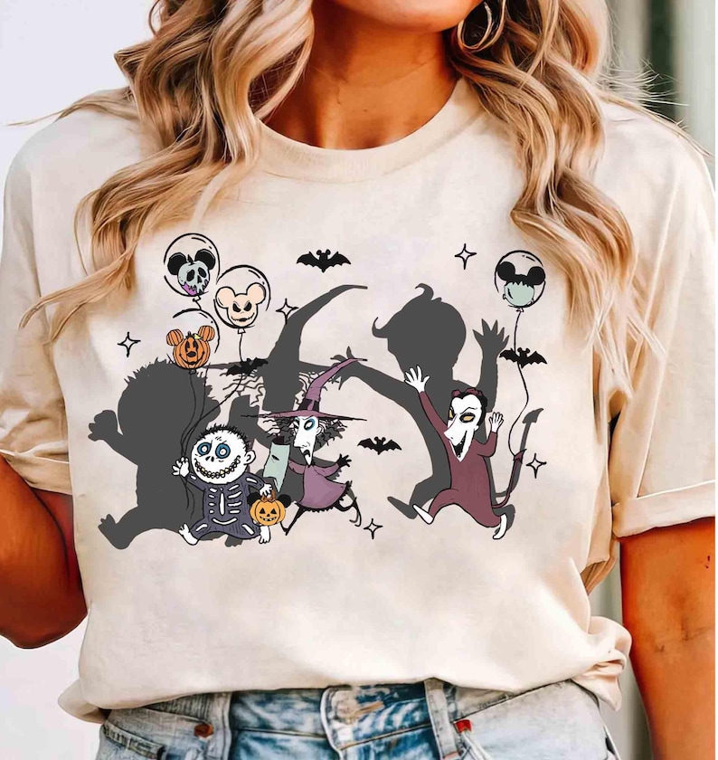 Puede incluir: Camiseta color crema con un gr&aacute;fico tem&aacute;tico de Halloween. El dise&ntilde;o incluye personajes de dibujos animados, murci&eacute;lagos, globos con caras de calaveras y Mickey Mouse, y estrellas. Los personajes est&aacute;n en varias poses, creando un aspecto l&uacute;dico y festivo.