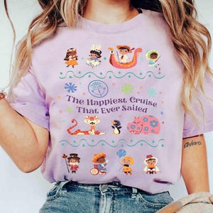 May include: A light purple t-shirt featuring the text "The Happiest Cruise That Ever Sailed" with colorful cartoon characters and decorative elements. The shirt has short sleeves and a crew neck.