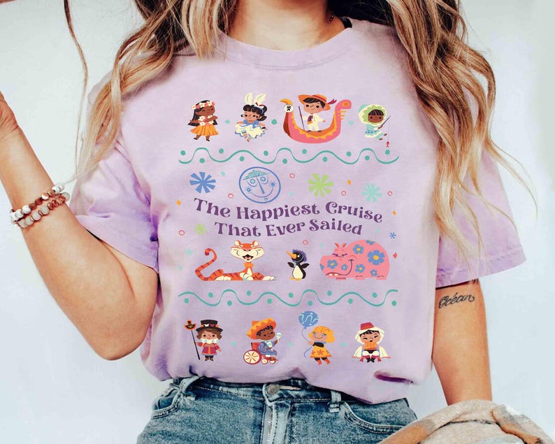 May include: A light purple t-shirt featuring the text "The Happiest Cruise That Ever Sailed" with colorful cartoon characters and decorative elements. The shirt has short sleeves and a crew neck.