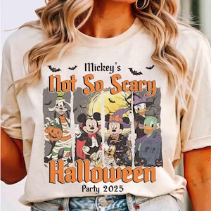 May include: Beige t-shirt featuring a Halloween design with Mickey Mouse, Minnie Mouse, Goofy, Donald Duck, and Daisy Duck in costumes. The text reads "Mickey's Not So Scary Halloween Party 2025" with bats.