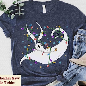 May include: Heather navy Bella T-shirt featuring a whimsical cartoon character wrapped in colorful Christmas lights, holding a candy cane and a small pumpkin. The design includes stars and snowflakes. The shirt is paired with blue jeans and a boot.