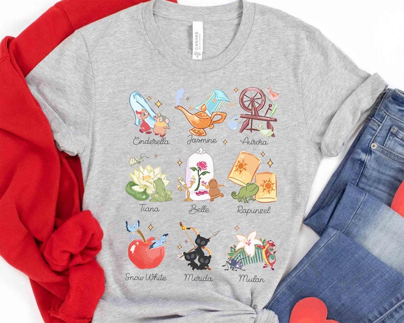 May include: A light gray t-shirt featuring colorful illustrations of Disney princesses and their associated icons, including Cinderella, Jasmine, Aurora, Tiana, Belle, Rapunzel, Snow White, Merida, and Mulan. The names of the princesses are printed below each image.