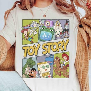 Puede incluir: Camiseta color crema con un gr&aacute;fico colorido de personajes de Toy Story al estilo c&oacute;mic. El dise&ntilde;o incluye a Buzz Lightyear, Woody, Rex y otros, con las palabras "TOY STORY" en letras amarillas grandes.