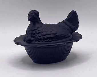 May include: A black hen-shaped covered dish. The hen sits atop a scalloped, fluted base. The lid is shaped like a hen with detailed feathers. The dish is made of a matte black material.