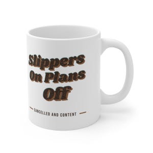 May include: A white ceramic mug featuring the dark brown text Slippers On Plans Off in a bold, retro-inspired font. Below the main text, the phrase CANCELLED AND CONTENT is printed in smaller, capitalized letters between two horizontal lines.