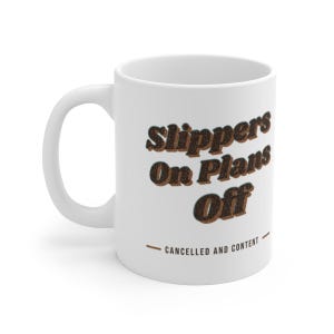 May include: A white ceramic mug featuring the dark brown text Slippers On Plans Off in a bold, retro-inspired font. Below the main text, a smaller line reads CANCELLED AND CONTENT in a simple sans-serif font, flanked by two horizontal brown lines.