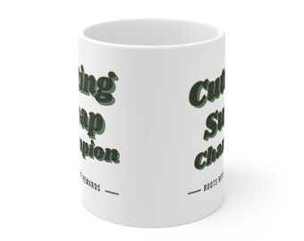 May include: A white ceramic mug featuring the dark green text "Cutting Soap Champion" in a retro font, with the smaller text "ROOTS BEFORE REWARDS" printed below it, accompanied by two horizontal green lines on either side of the phrase.