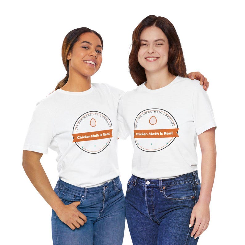 Pu&ograve; includere: Una t-shirt bianca a maniche corte con una grafica circolare che include una piccola icona a forma di uovo, il testo "JUST ONE MORE HEN, I PROMISE" lungo il bordo superiore e un banner arancione al centro con il testo "Chicken Math Is Real".