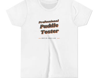 May include: A white short-sleeved t-shirt featuring the text Professional Puddle Tester in a dark grey font with an orange drop shadow. Below the text, a horizontal line separates the phrase BOOTS ON, GIGGLES LOUD in a smaller dark grey font.