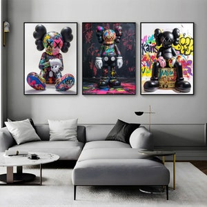 May include: Three colourful framed prints featuring black and white cartoon figures with graffiti backgrounds. The figures are wearing red and white X-shaped eyes and have a black and white paint splatter design. The prints are framed in black and have a white mount.