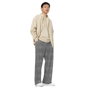 Könnte beinhalten: Eine Person trägt ein beiges Button-Down-Hemd über einem beigen T-Shirt, kombiniert mit einer Hose mit schwarz-weißem Muster. Die Hose hat ein sich wiederholendes geometrisches Design. Die Person trägt weiße Turnschuhe.