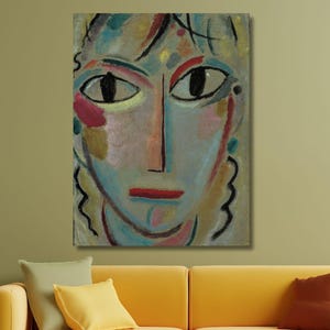 Puede incluir: Pintura abstracta de un rostro con ojos grandes y oscuros, labios rojos y una nariz larga. La obra presenta una paleta de azules, rosas y amarillos, con contornos negros. La pintura cuelga sobre un sofá amarillo con cojines decorativos.