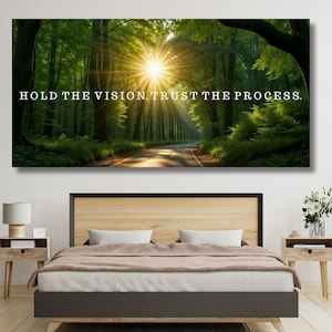 Könnte beinhalten: Ein großer rechteckiger Leinwanddruck mit einer Waldszene und einer Straße, die zu einer hellen Sonne führt. Der Text "HOLD THE VISION, TRUST THE PROCESS" ist in Weiß dargestellt. Der Druck hängt über einem Bett in einem Schlafzimmer.