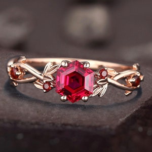 May include: A rose gold ring featuring a red ruby gemstone and intricate leaf details.