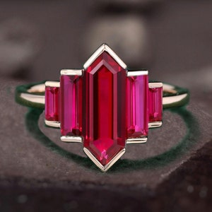 May include: A gold ring with a large, rectangular, red ruby gemstone surrounded by smaller, rectangular, red ruby gemstones.