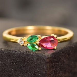 May include: A gold ring featuring a red pear-shaped gemstone and two green pear-shaped gemstones.