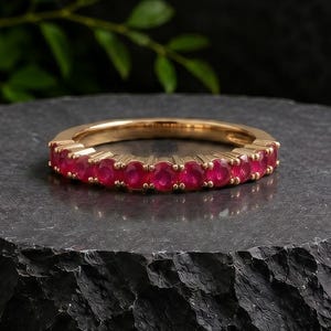 Peut inclure: Une bague en or avec une rangée de rubis rouges vifs de taille ronde sertis sur la moitié avant de l'anneau. La bague est présentée horizontalement, mettant en valeur la taille uniforme et la couleur rouge profond des pierres.