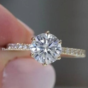 May include: A gold engagement ring with a large, round, clear center stone and a band of smaller, clear stones.