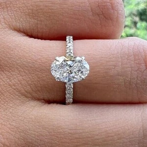 May include: A silver engagement ring featuring an oval-shaped diamond centre stone and a pave diamond band.