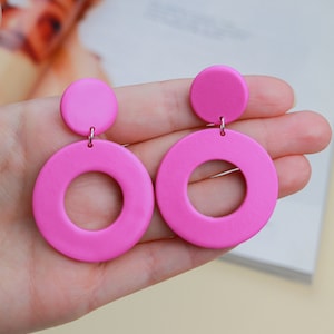 Könnte beinhalten: Ein Paar rosa Statement-Ohrringe mit großen, runden, hohlen Formen. Die Ohrringe haben einen kleineren, festen Kreis oben.