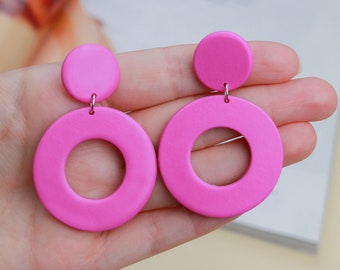 May include: A pair of pink statement earrings with large, round, hollow shapes. The earrings have a smaller, solid circle at the top.