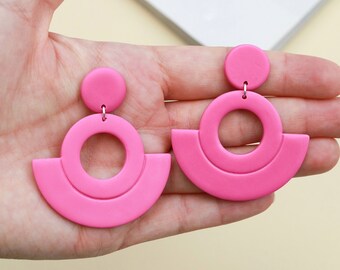 May include: A pair of pink geometric earrings with a large circle and a half-circle design.