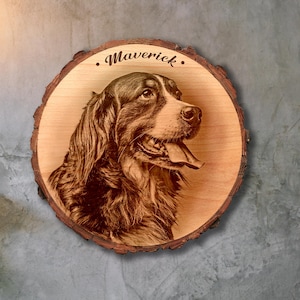 Puede incluir: Placa de madera redonda con un retrato grabado con láser de un perro, con el nombre "Maverick" en la parte superior. El perro es marrón y blanco, con la lengua fuera. La placa tiene un borde de corteza natural.