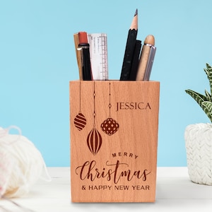 May include: A personalised wooden desk tidy with a Christmas theme. It features a red and white striped bauble, a red bauble with white polka dots, and the text "Merry Christmas & Happy New Year". The organiser is engraved with the name "Jessica".