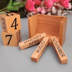 May include: Wooden calendar with a cube design. The calendar has numbers 3, 4, 7, and 1. The months are January, April, August, July, and November.