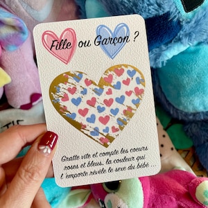 Peut inclure: Une carte rectangulaire blanche avec le texte Fille ou Garçon ? accompagné d'un cœur rose et d'un bleu. Au centre, un grand cœur à gratter doré recouvre un motif de petits cœurs roses et bleus, avec du texte explicatif en dessous.