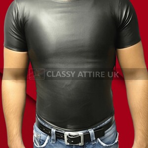 May include: A black, short-sleeved shirt with a crew neck. The shirt is made of a shiny material and is paired with blue jeans and a black belt with a silver buckle. The text "CLASSY ATTIRE UK" is visible.