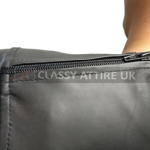 May include: Close-up of a black leather garment with a zipper closure. The garment appears to be a top or a dress, with visible stitching and a smooth texture. The text "CLASSY ATTIRE UK" is printed on the garment.
