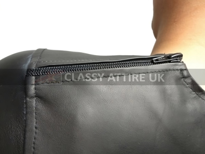 May include: Close-up of a black leather garment with a zipper closure. The garment appears to be a top or a dress, with visible stitching and a smooth texture. The text "CLASSY ATTIRE UK" is printed on the garment.