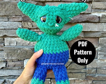 May include: A green and blue crocheted goblin doll with large pointed ears, dark glossy eyes, and a small white tooth. The text reads Goblin Crochet Pattern and PDF Pattern Only. The doll has a textured yarn finish with a two-tone color scheme.