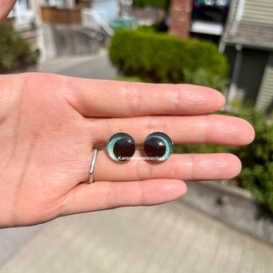 K&ouml;nnte beinhalten: Zwei schwarze und gr&uuml;ne Glasaugen mit silbernem Glitzerakzent. Die Augen haben einen Durchmesser von etwa 2,5 cm.