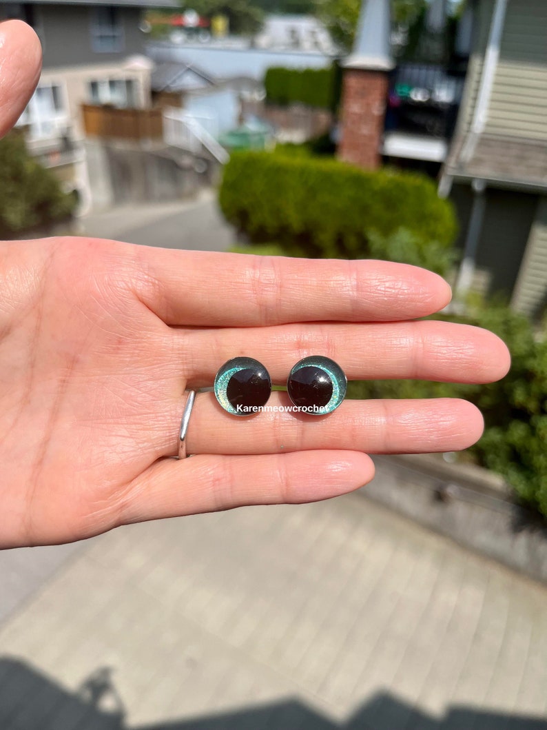 K&ouml;nnte beinhalten: Zwei schwarze und gr&uuml;ne Glasaugen mit silbernem Glitzerakzent. Die Augen haben einen Durchmesser von etwa 2,5 cm.