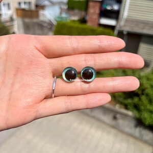 K&ouml;nnte beinhalten: Zwei runde, schwarze und gr&uuml;ne Sicherheitsaugen mit schimmerndem Finish. Die Augen haben einen Durchmesser von etwa 2,5 cm.