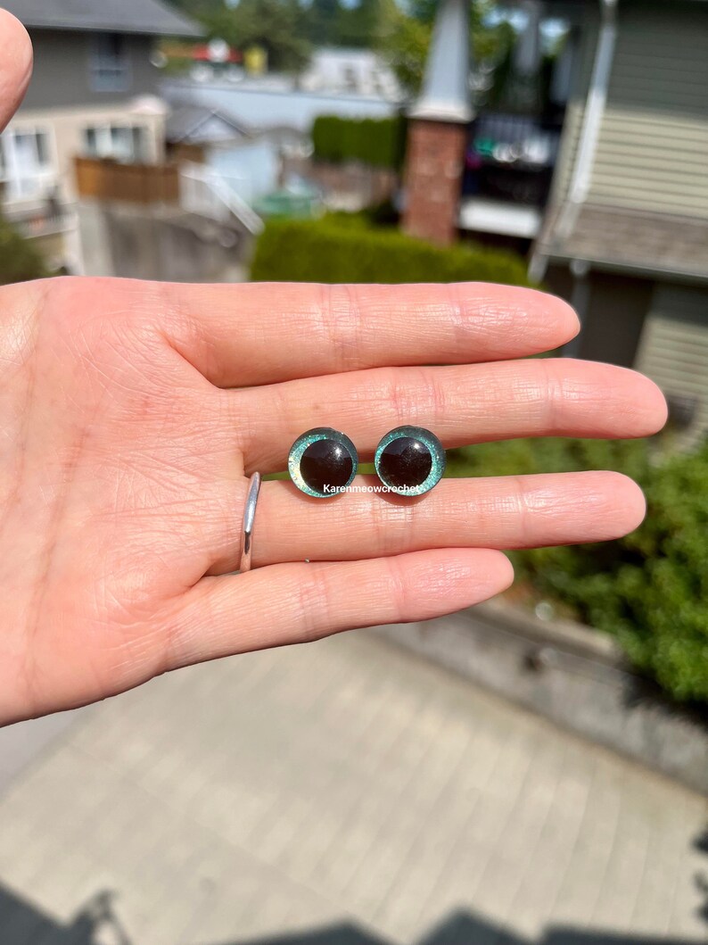 K&ouml;nnte beinhalten: Zwei runde, schwarze und gr&uuml;ne Sicherheitsaugen mit schimmerndem Finish. Die Augen haben einen Durchmesser von etwa 2,5 cm.