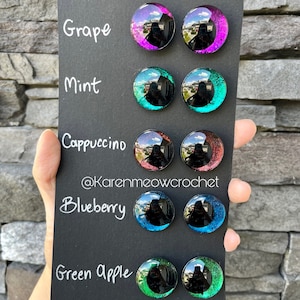 May include: A black card with five rows of colourful round glass eyes. Each row is labelled with a colour name: Grape, Mint, Cappuccino, Blueberry, and Green Apple. The card is held in a hand.