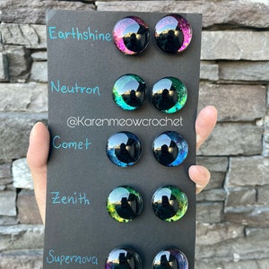 May include: A black card with five rows of colourful glass eyes. Each row is labelled with a name: Earthsine, Neutron, Comet, Zenith, and Supernova. The eyes are all different colours and have a glittery finish.
