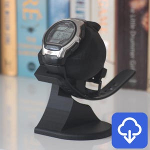 May include: A black 3D printed watch stand with a curved base and a raised platform to hold a watch. The stand is designed to hold a watch with a round face and a strap.