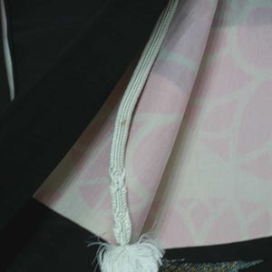 K&ouml;nnte beinhalten: Ein schwarzer Kimono mit einer wei&szlig;en Schnur und Quaste. Der Kimono hat ein rosa-wei&szlig;es Blumenmuster auf der Innenseite.