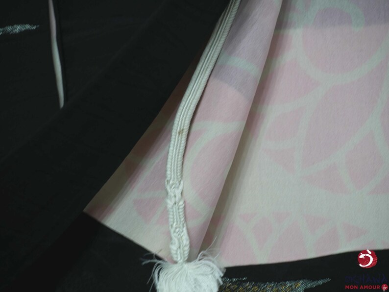 K&ouml;nnte beinhalten: Ein schwarzer Kimono mit einer wei&szlig;en Schnur und Quaste. Der Kimono hat ein rosa-wei&szlig;es Blumenmuster auf der Innenseite.