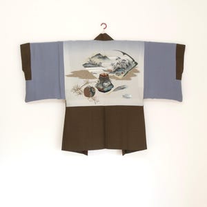May include: A traditional Japanese kimono with a landscape design. The kimono features a light blue body with brown sleeves and a brown collar. The back panel displays a detailed illustration of mountains, trees, and an inkwell.