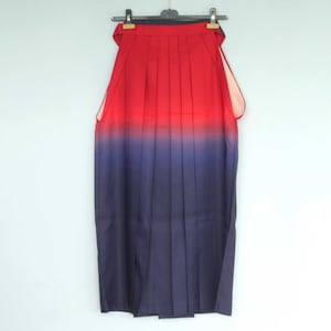 May include: A red and blue ombre hakama, a traditional Japanese garment, hangs on a hanger against a white background.