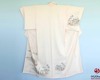 Könnte beinhalten: Ein blasses rosa japanisches Kimono mit einem traditionellen Design aus Bäumen und Bergen, das in Grün- und Grautönen gestickt ist.