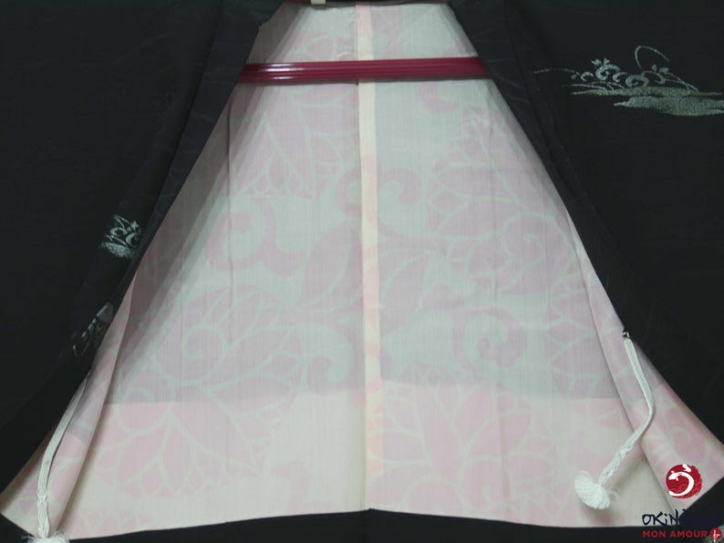 K&ouml;nnte beinhalten: Ein schwarzer Kimono mit einem rosa floralen Musterfutter. Der Kimono hat eine wei&szlig;e Schnur und ein silbernes Design auf dem schwarzen Stoff.