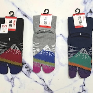 Può includere: Tre paia di calze tabi con un design a punta divisa. Le calze presentano una stampa di montagna con diverse combinazioni di colori: rosso, verde e blu. Le calze sono realizzate in un materiale morbido e confortevole e sono perfette per l'uso quotidiano.