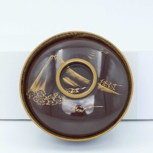 May include: A dark red Japanese bowl with a gold rim and a gold design of a mountain and clouds. The bowl is made of lacquered wood.