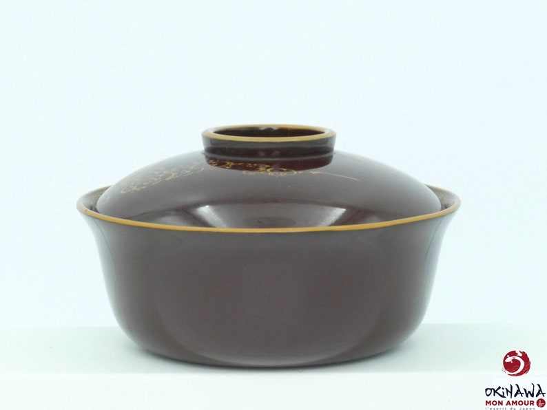 May include: A dark brown ceramic bowl with a lid. The bowl has a gold rim and a subtle gold design. The lid has a gold rim and a gold design.